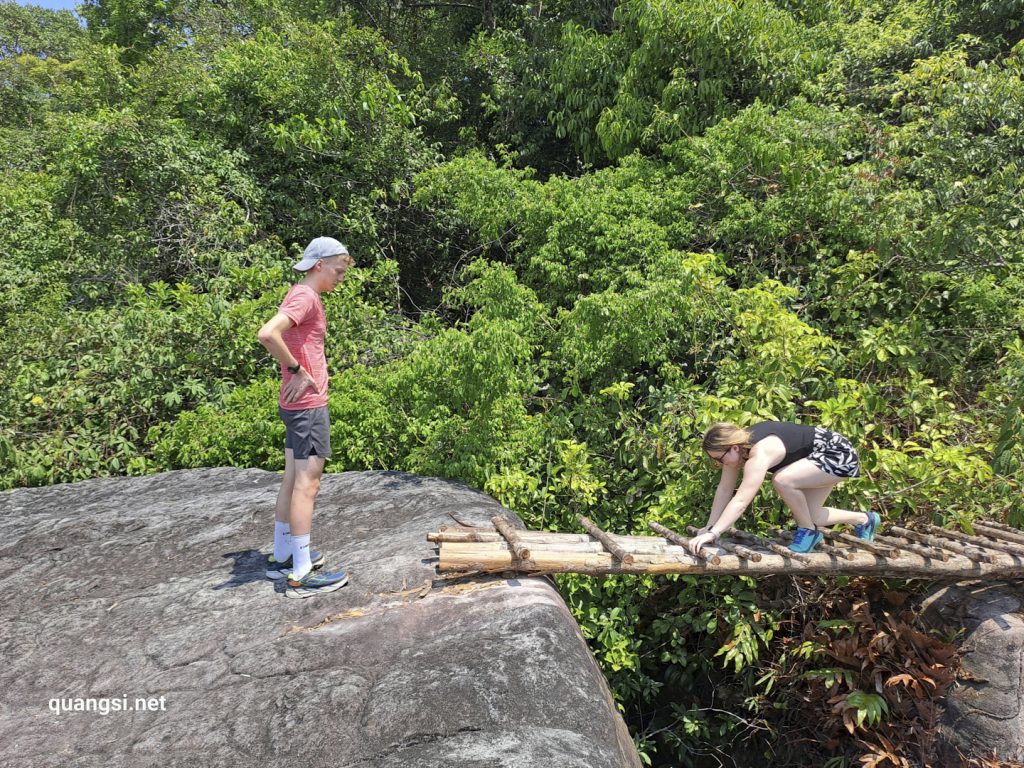 a man and woman standing on a log bridge over a rock