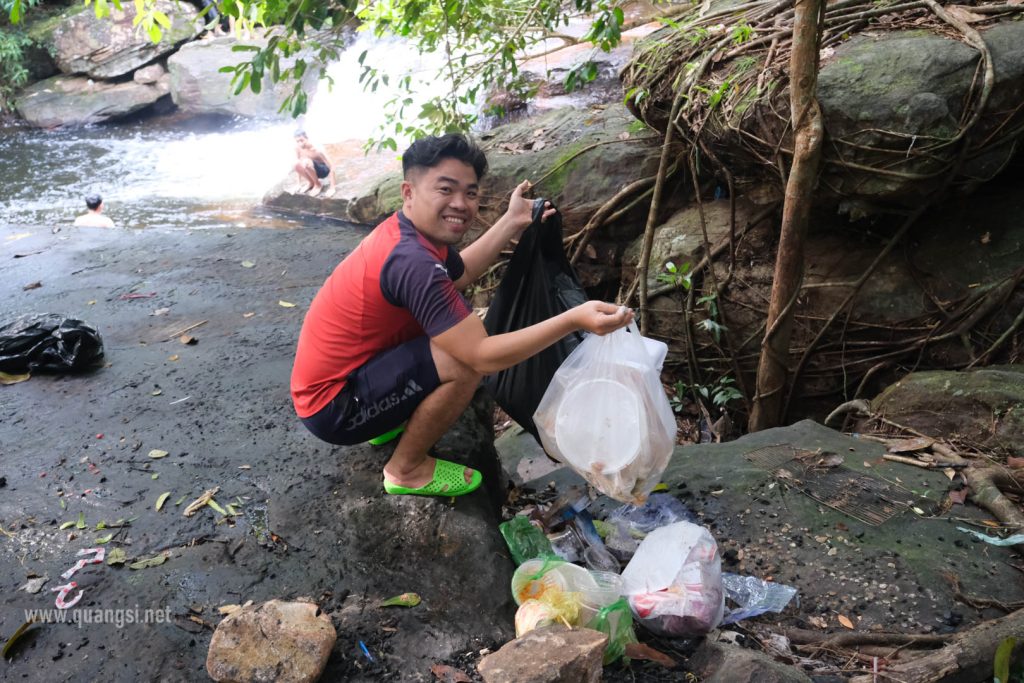 a man squatting on a rock with a bag of trash