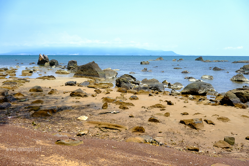 a rocky beach with water and mountains in the background